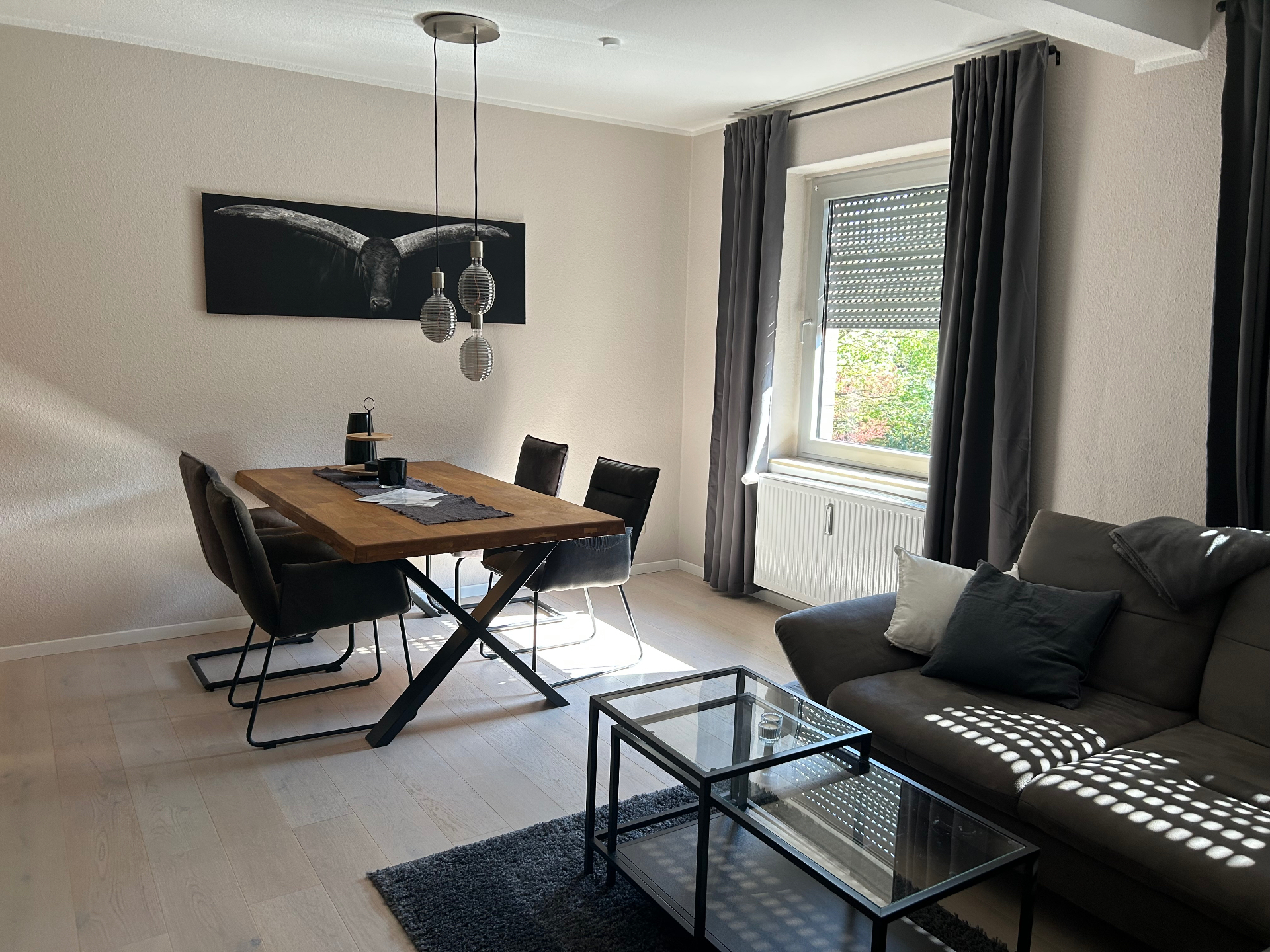 Helles Wohn-Esszimmer mit Holztisch, Sofa und großem Fenster